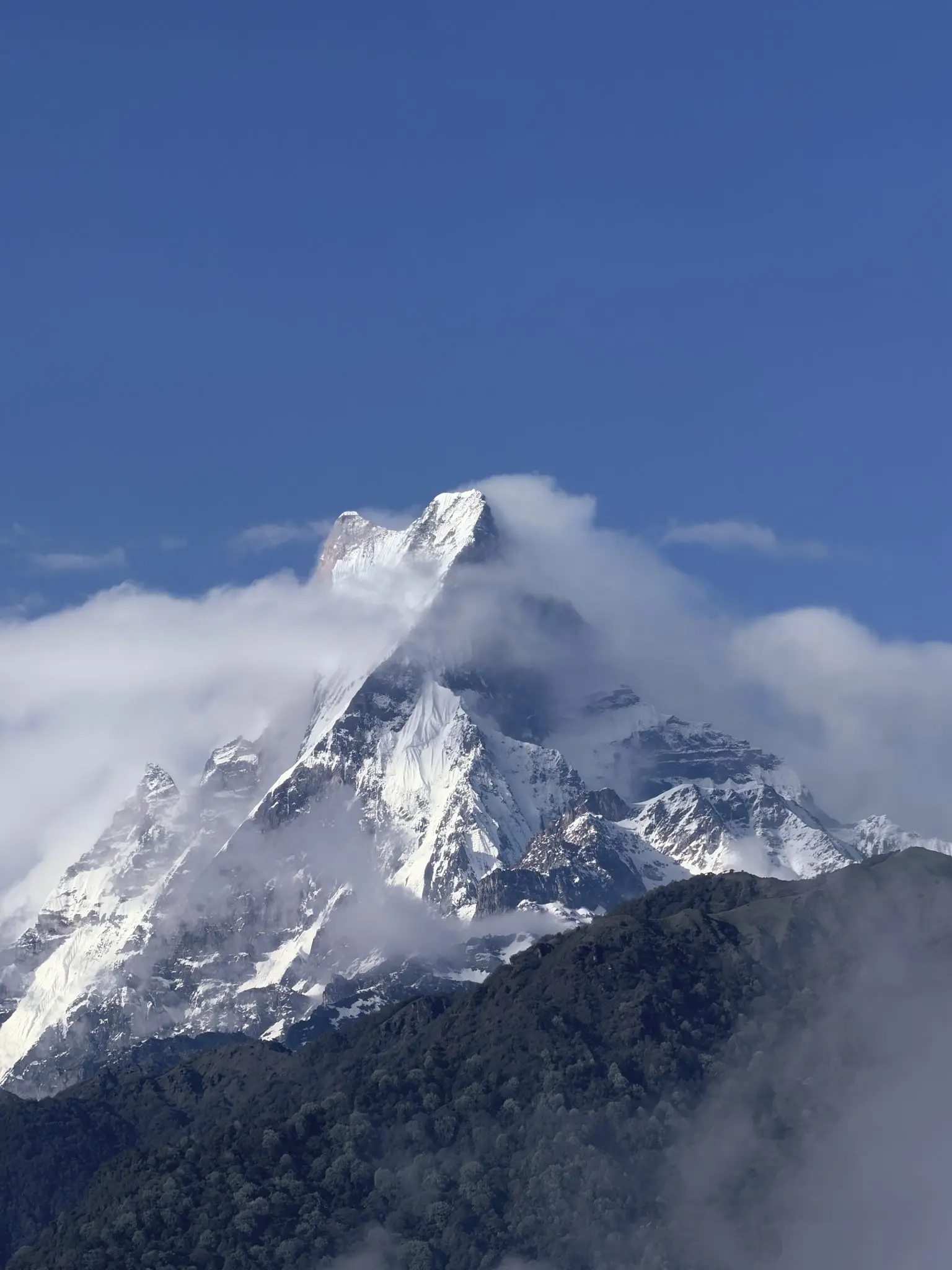 Snow-capped Machapuchare (Fish Tail) mountain peak against blue sky and low cloud.