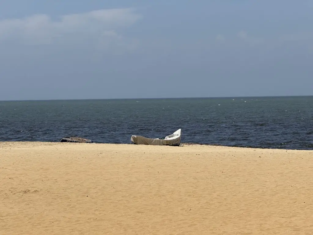 Golden sandy beach with a calm blue ocean, clear sky, and a covered boat resting on the sand.